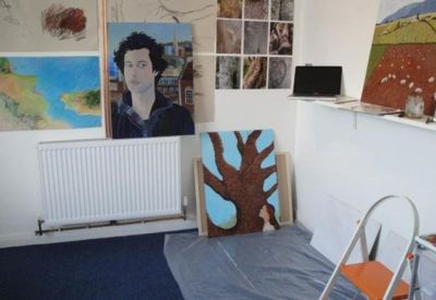 Creative studio space featuring various art canvases on walls and a bright painting of a tree.
