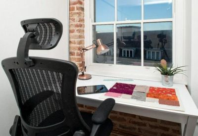 Close-up of a white desk with fabric samples, a copper lamp, and a view through a sash window.