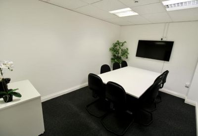 Private meeting room with a white square table, black chairs, a wall-mounted TV, and a green plant.