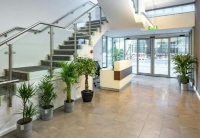 Bright reception area with a modern desk, indoor plants, and a glass staircase.