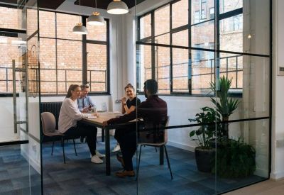 Modern glass-walled meeting room with people seated around a wooden table.