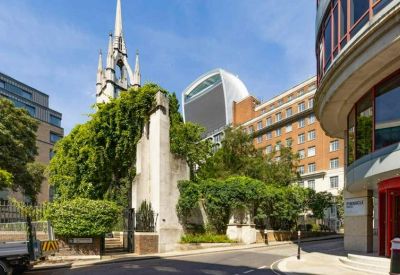 Street view featuring an ivy-covered stone wall and a historic church spire in the background.