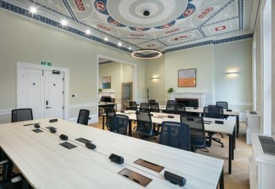 Bright open-plan office featuring long white desks and a decorative tiled ceiling.