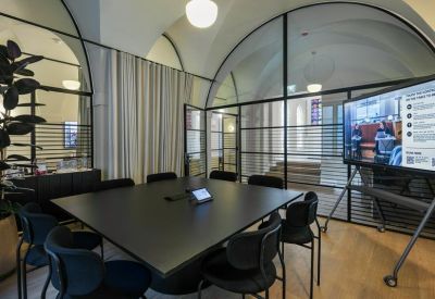 Modern meeting room with a large black table, glass partitions, and arched ceilings.