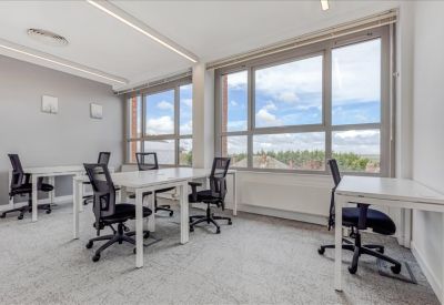 Bright workspace featuring several desks and large windows overlooking trees.