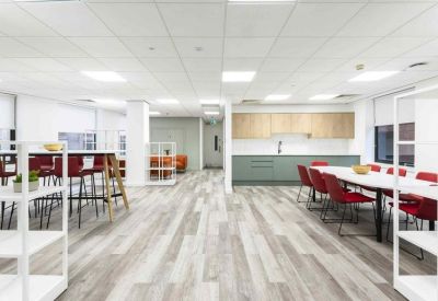 Spacious communal kitchen and dining area with red chairs and light wood cabinetry.