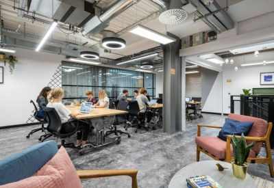 Open-plan office with teams working at long wooden desks under modern circular lighting.