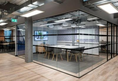 Glass-walled meeting room with a large white table and grey chairs under industrial ceilings.