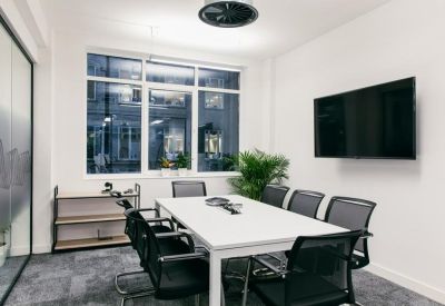Bright meeting room with white table, black mesh chairs, and wall-mounted TV.