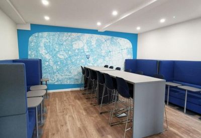 Bright breakout area featuring high tables, blue privacy booths, and a large blue wall mural.