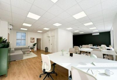 Spacious office area featuring white workstations, wooden flooring, and a lounge corner.