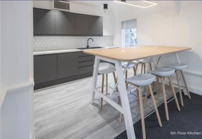 Bright kitchen and breakout area with a large wooden high-top table and stools.