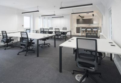 Spacious open-plan office with white desks, black ergonomic chairs, and linear pendant lighting.