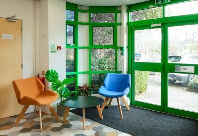 Bright reception seating area with green window frames and colorful modern chairs.