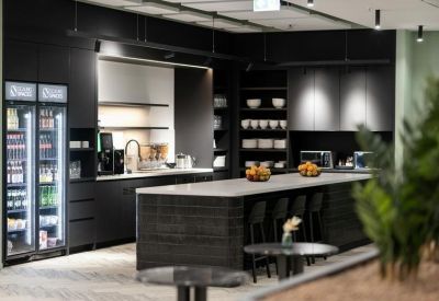 Modern black kitchen and breakout area with a large island, stools, and stocked refreshment fridges.