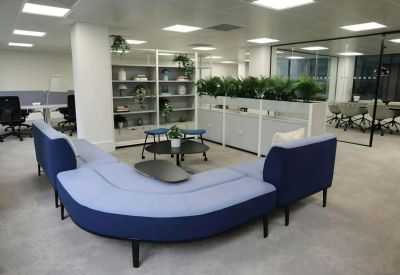 Breakout area featuring a large curved blue sofa and low coffee tables.