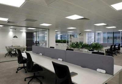 Open-plan office with white desks, black chairs, and a plant-lined partition.
