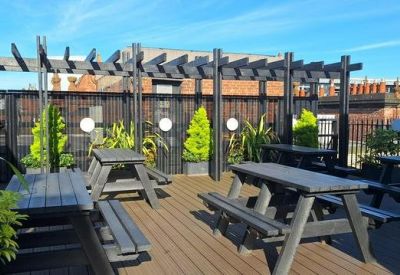 Outdoor roof terrace with wooden decking, picnic tables, and a black pergola.