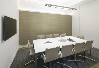 Minimalist boardroom with a large white table, tan chairs, and wall-mounted screen.