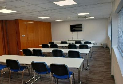 Classroom-style training room with rows of white desks and black chairs.