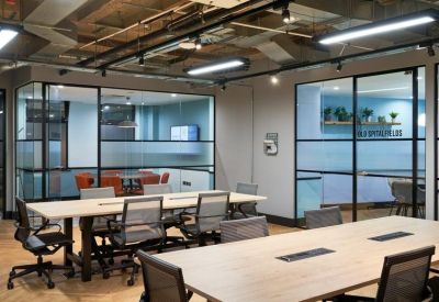 Open-plan office with long wooden desks, ergonomic chairs, and glass partitions.