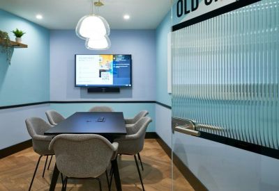 Small meeting room with blue and white walls, a black table, and a wall-mounted screen.