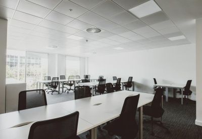 Bright open-plan office space with rows of white desks and black ergonomic chairs.