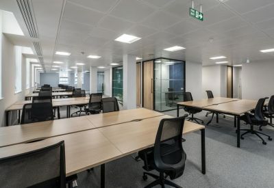 Spacious open-plan office with rows of light wood desks and ergonomic black chairs.