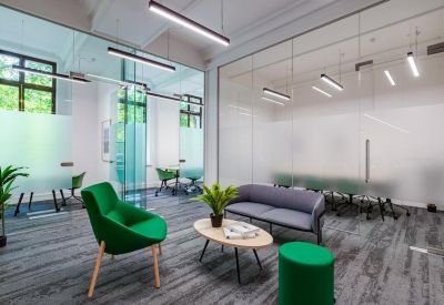 Breakout lounge area with a green velvet armchair, grey sofa, and glass partitions.