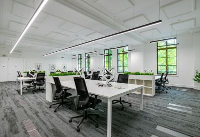 Spacious workspace featuring long white communal desks and modern linear overhead lighting.