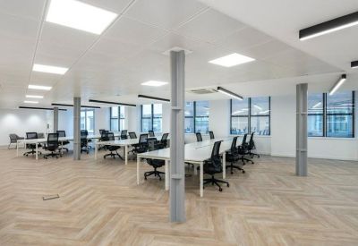 Bright office floor featuring several white desk clusters and industrial-style support columns.