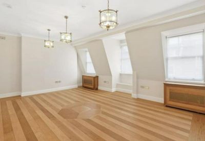 Spacious office room with wooden floors, neutral walls, and large windows with wooden radiator covers.