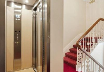 Elevator lobby with a modern lift and red carpeted stairs with ornate white railings.