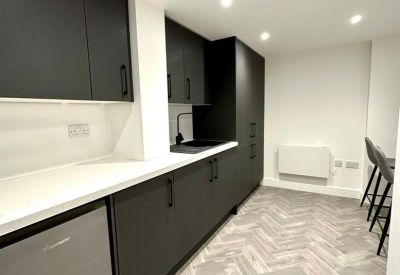 Modern communal kitchen with dark grey cabinetry and herringbone wood flooring.