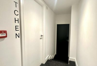 Bright hallway with white walls and a kitchen entrance sign.