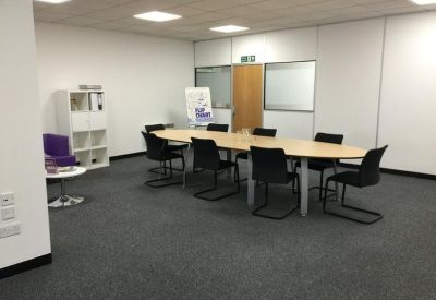 Bright conference room with a large light wood oval table and black chairs.