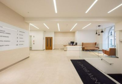 Modern reception area with a white front desk, directory board, and tan leather seating.