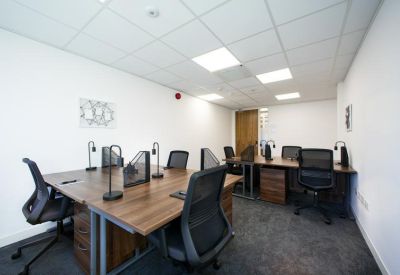 Bright open-plan workspace featuring multiple wooden desks with task lamps and mesh chairs.