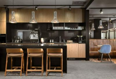 Sleek office kitchen and coffee bar with wooden cabinetry and black marble island.
