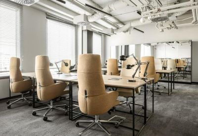 Close-up of wooden desks and tan office chairs in a light-filled workspace.