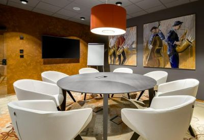 Circular meeting room with white tub chairs, a wooden feature wall, and jazz-themed artwork.