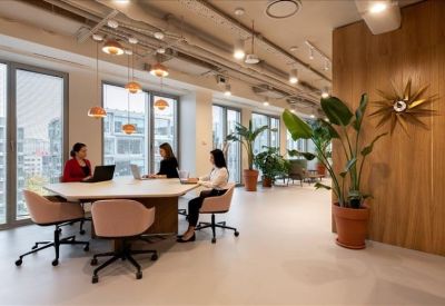 Modern coworking lounge with several round tables, pink chairs, and lush potted plants.