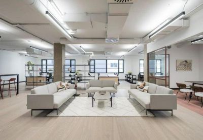 Spacious communal lounge featuring grey sofas, a white patterned rug, and industrial ceilings.