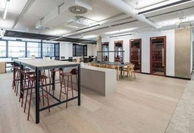 High-top collaboration table with bar stools adjacent to private glass-fronted phone booths.