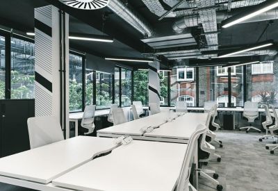 Modern open-plan workspace with white desks and industrial ceiling.