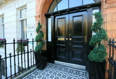 The black gloss front entrance featuring manicured topiary trees and a mosaic tile doorstep.