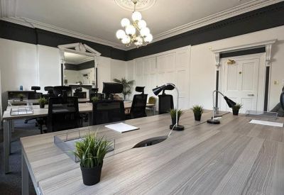 Bright open-plan office suite with rows of modern black mesh chairs and light wood desks.