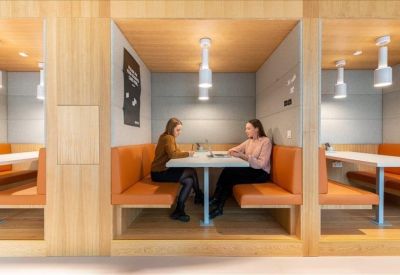 Wooden semi-private coworking booths with orange bench seating and white pendant lights.
