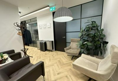 Lounge area with small round tables, high-back chairs, and a bright herringbone wood floor.