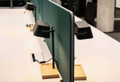 Row of desks divided by a teal screen with minimalist black desk lamps on wooden bases.